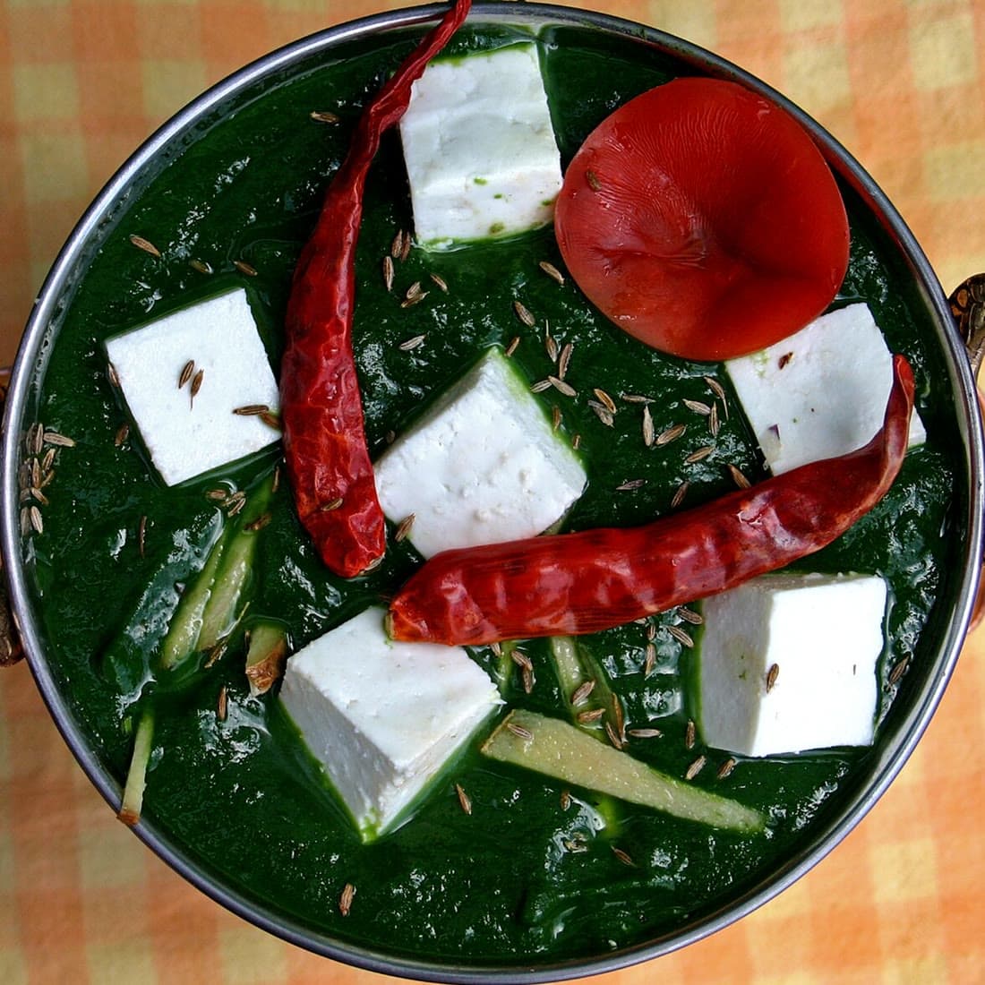 Palak paneer with cubes of paneer and red chilies in a steel kadai