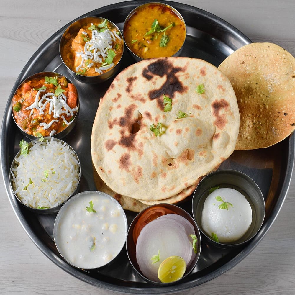 A steel thali with dal, paneer, rice, naan and papad